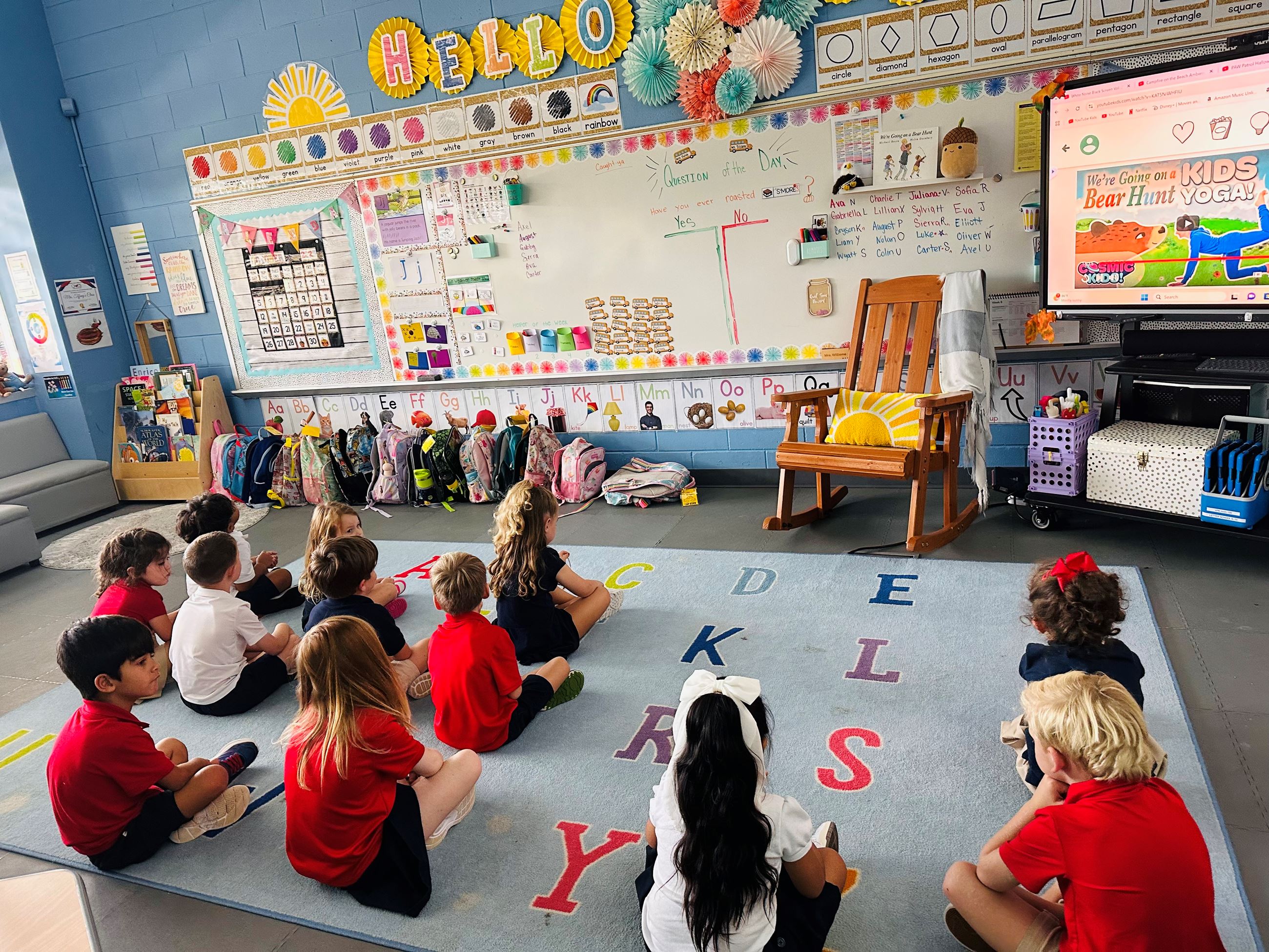 Several students seated on a rug in a classroom