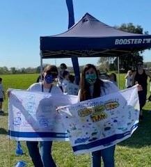 Two female teachers holding up their class Fun Run team flags outside in front of a Boosterthon tent